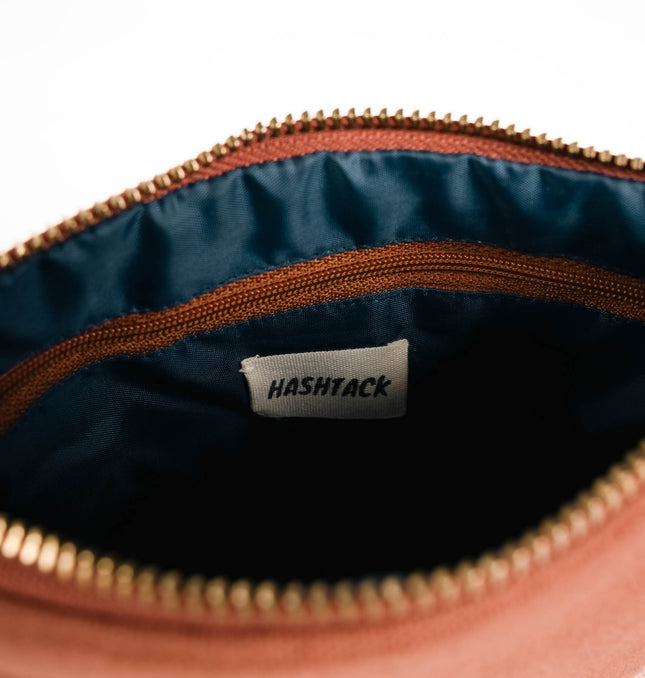 Side angle of terracotta brown utility pouch highlighting secure gold-tone metal zipper and wristlet strap