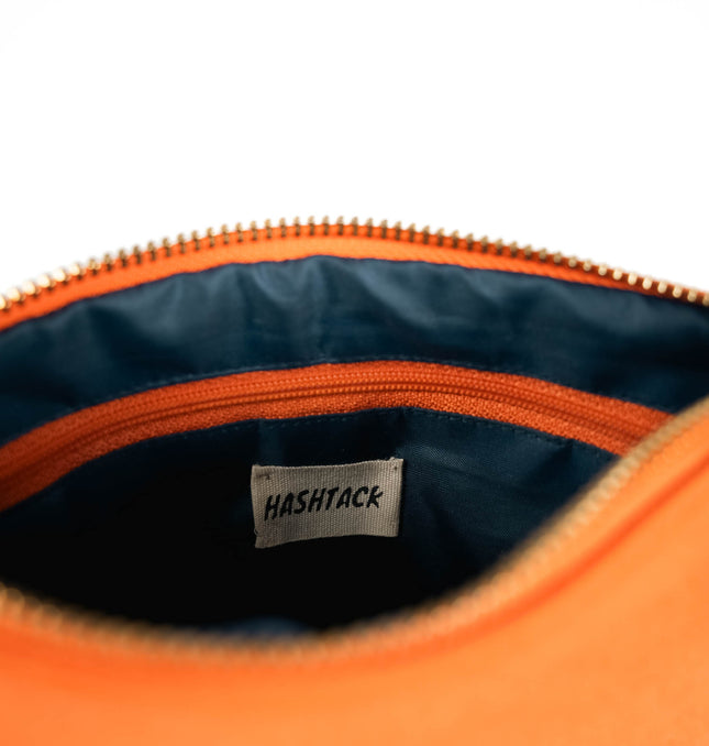 Side angle of bright orange utility pouch highlighting secure gold-tone metal zipper and wristlet strap