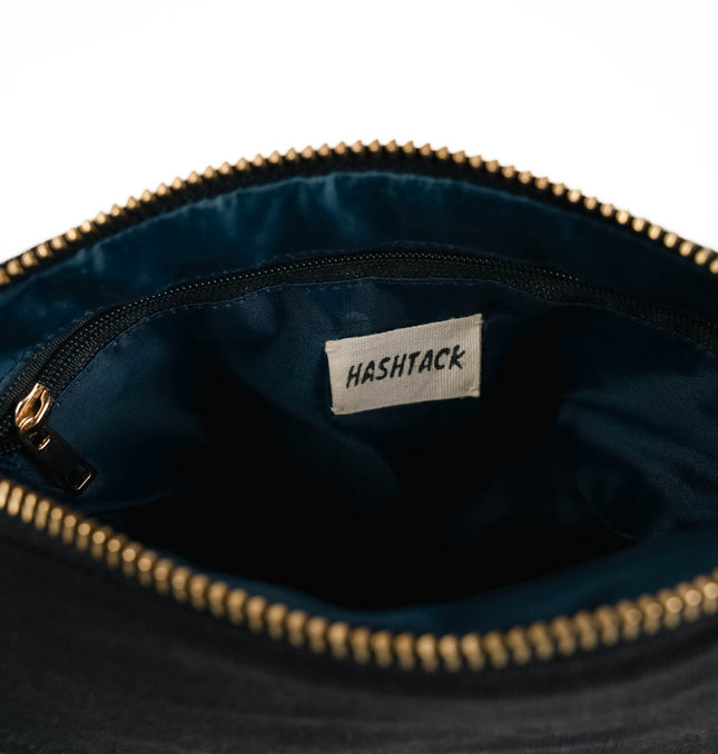 Side angle of black canvas utility pouch highlighting secure gold-tone metal zipper and wristlet strap