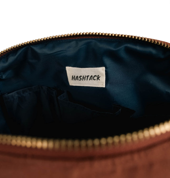 Side angle of terracotta canvas utility pouch highlighting secure gold-tone metal zipper and wristlet strap